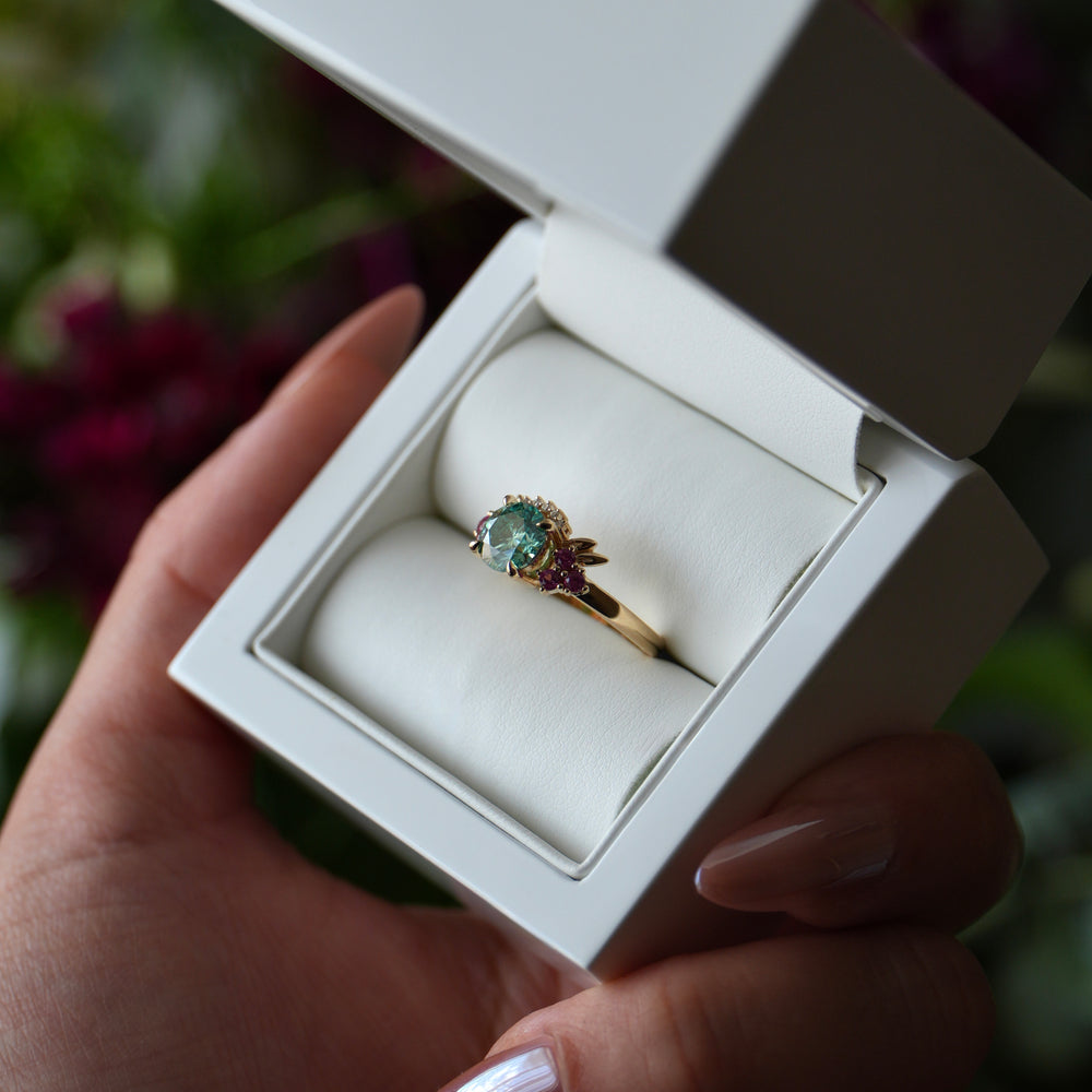 Gold ring with a green gemstone in a white box held by a hand.