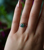 Hand wearing a ring with a green gemstone against a blurred natural background