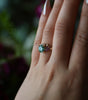 Hand wearing a ring with a green gemstone against a blurred background
