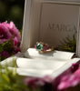Ring in a jewelry box with 'MARGA' branding, surrounded by pink flowers.