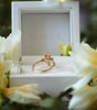 Gold ring in a white jewelry box with flowers around