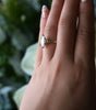 Hand wearing a ring with a diamond, set against a blurred natural background