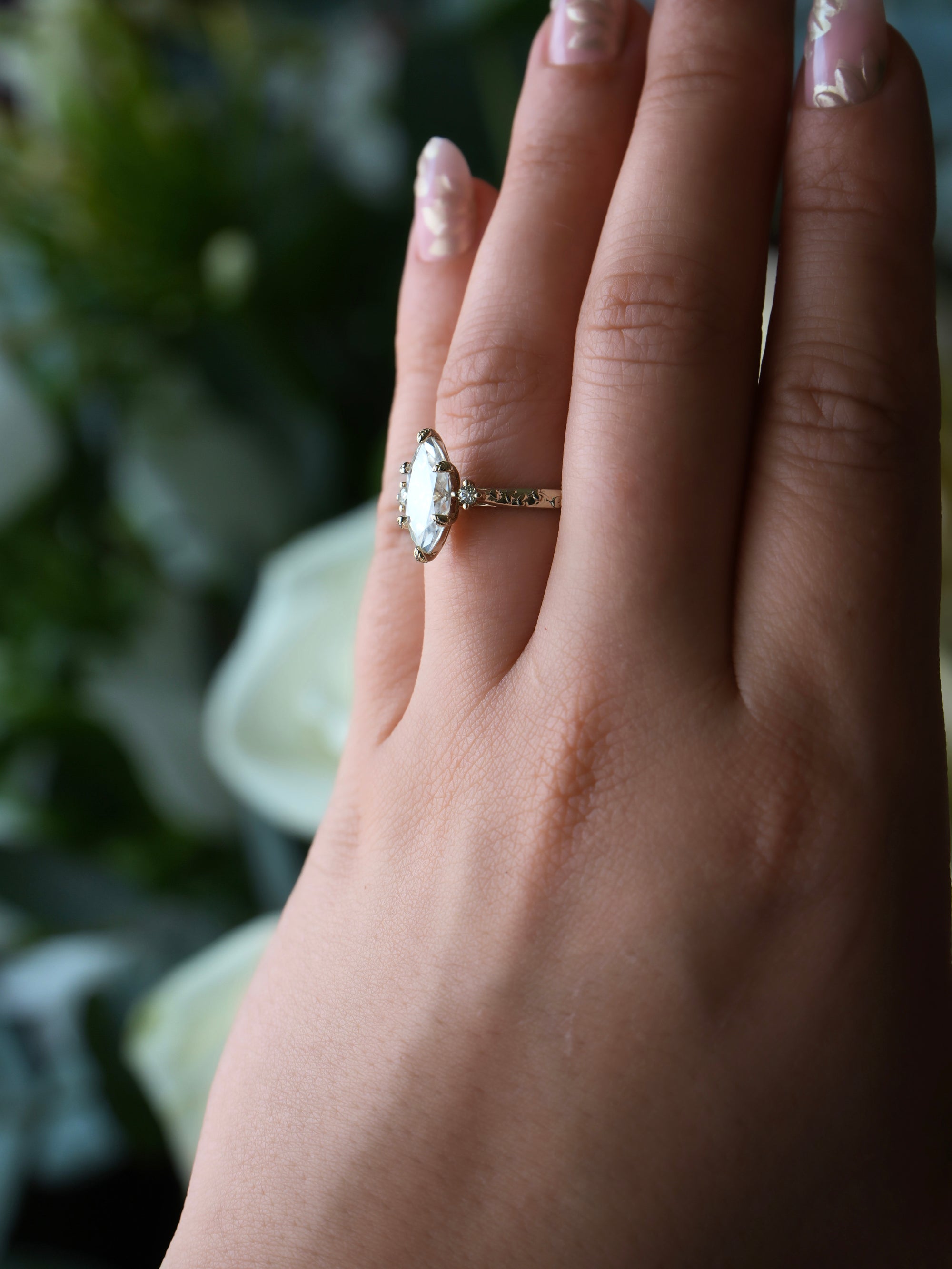 Hand wearing a ring with a diamond, set against a blurred natural background