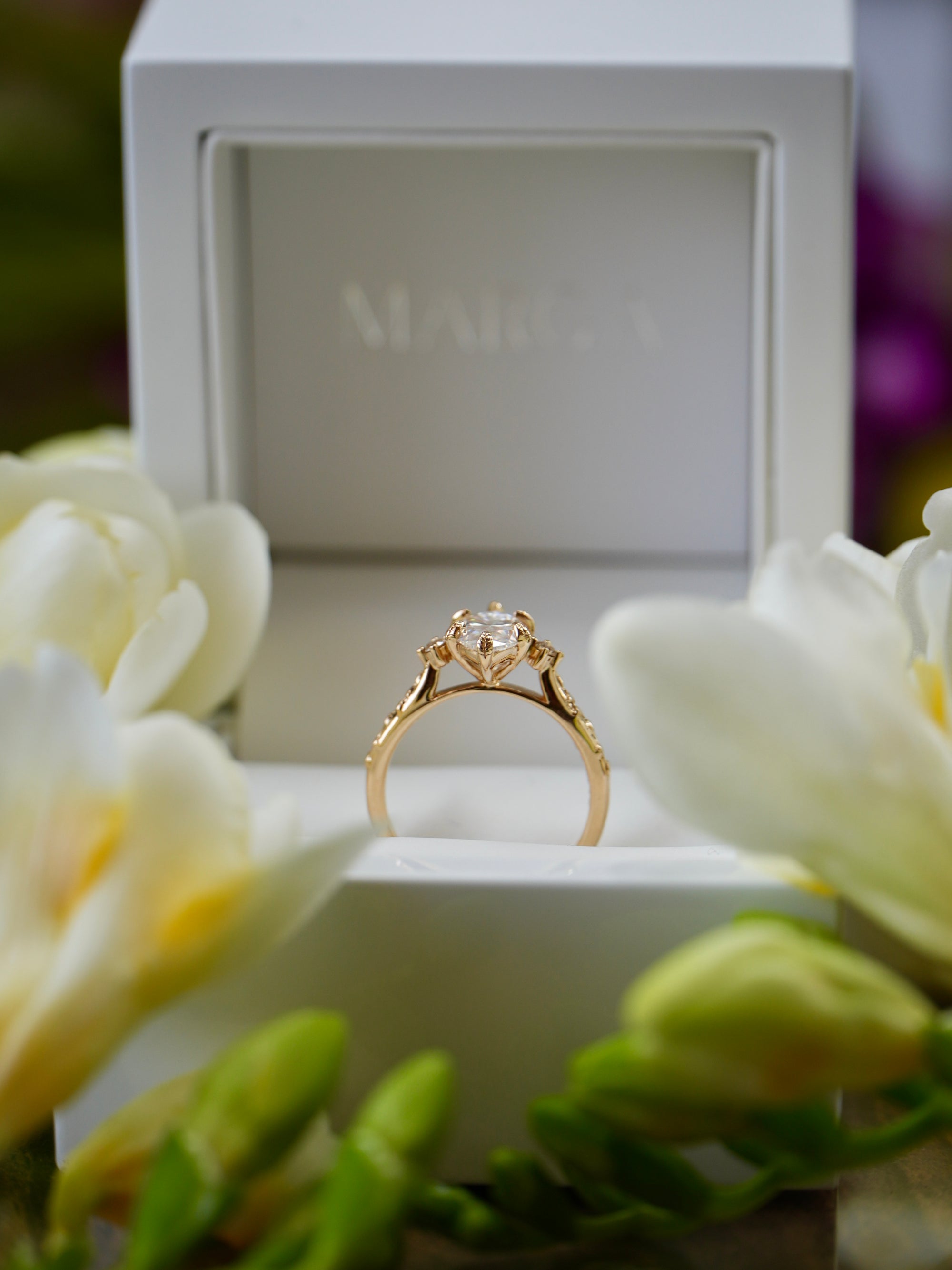 Gold ring on a white stand with white flowers and a blurred background