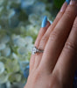 Close-up of a hand wearing a diamond ring with a blurred floral background
