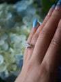 Close-up of a hand wearing a diamond ring with a blurred floral background