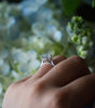 Close-up of a hand wearing a diamond ring with a blurred floral background