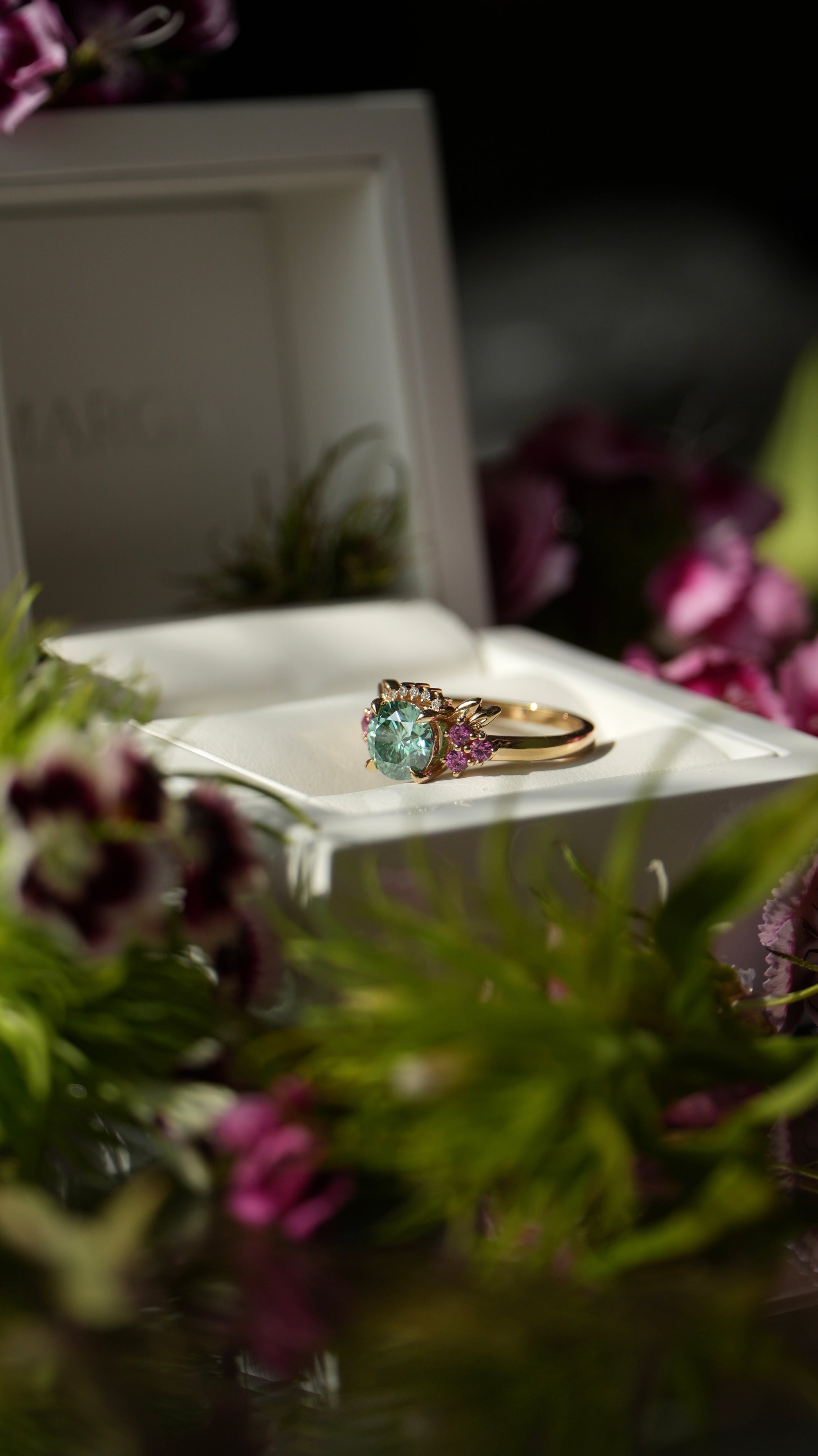 Gold ring with a green gemstone in a white box surrounded by flowers